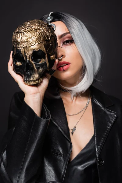 Mujer en traje de Halloween bruja celebración espeluznante cráneo de oro cerca de la cara aislado en negro - foto de stock