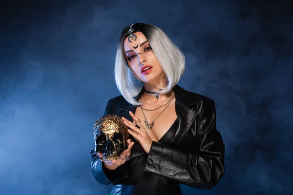 Sexy Frau im Halloween-Kostüm mit goldenem Totenkopf auf dunklem Hintergrund mit blauem Nebel — Stockfoto