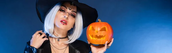 Ash blonde woman in pointed hat holding jack o lantern on blue background, banner — Stock Photo