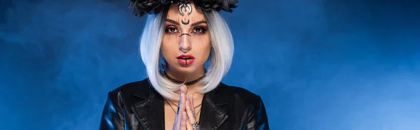 Mujer joven en maquillaje de Halloween bruja con las manos en oración fondo de niebla azul, pancarta - foto de stock