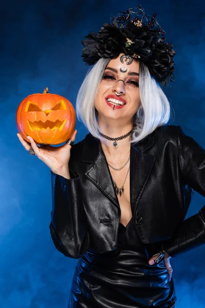 Mujer alegre en traje de bruja y el rostro con calabaza tallada cerca de la niebla azul - foto de stock