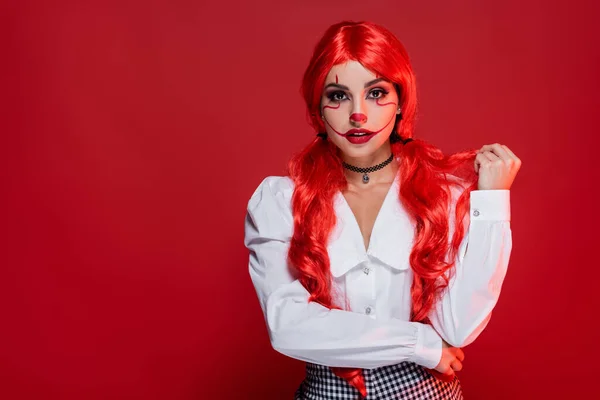 Молодая женщина с длинными волосами и клоунский макияж глядя на камеру изолированы на красный — стоковое фото