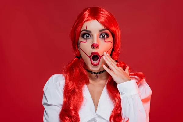 Вражена жінка з макіяжем на Хеллоуїн торкається обличчя і дивиться на камеру ізольовано на червоному — стокове фото