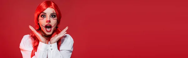 Excited woman with bright colored hair holding hands near face and looking at camera isolated on red, banner — Stock Photo