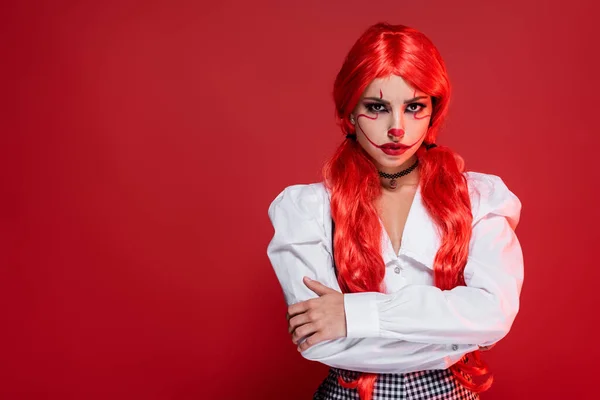 Donna offesa con code di cavallo luminose e trucco da clown in piedi con braccia incrociate isolate su rosso — Foto stock