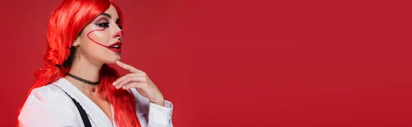 Giovane e premurosa donna con capelli brillanti e trucco da clown che tocca il mento isolato su rosso, banner — Foto stock