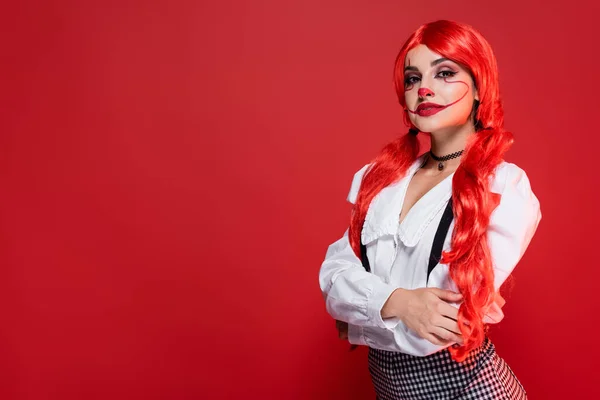 Жінка з яскравим кольоровим волоссям і макіяжем на Хеллоуїн позує схрещеними руками ізольовано на червоному — стокове фото