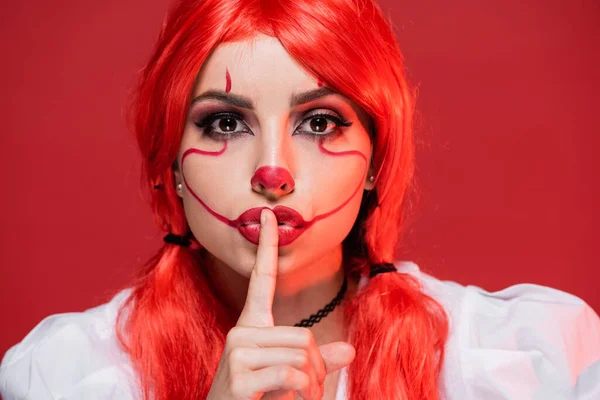 Mujer joven con el pelo brillante y el maquillaje de Halloween mostrando signo de silencio aislado en rojo - foto de stock