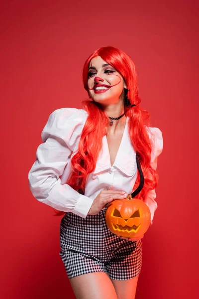 Feliz mujer en halloween maquillaje celebración jack o linterna aislado en rojo - foto de stock