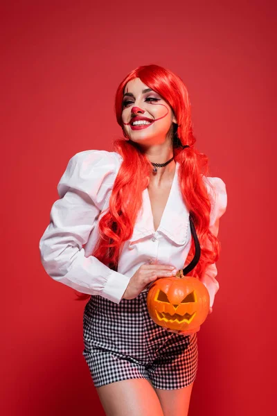 Happy woman in halloween makeup holding jack o lantern isolated on red — Stock Photo