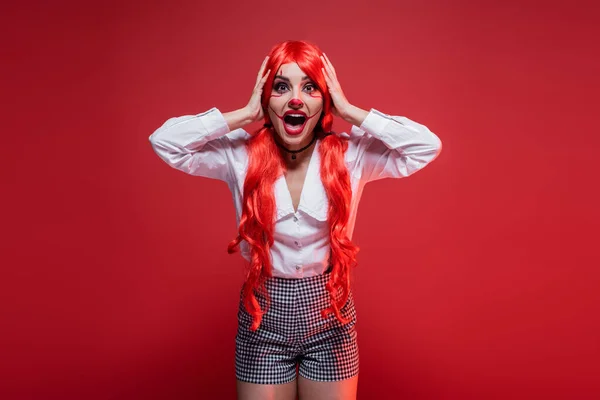 Femme choquée dans halloween maquillage touchant les cheveux colorés et hurlant isolé sur rouge — Photo de stock