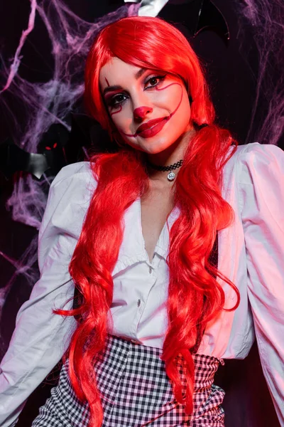 Redhead woman with ponytails and clown makeup looking at camera on black background with spiderweb — Stock Photo