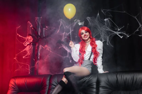 Mujer feliz con maquillaje de payaso y globo amarillo mirando a la cámara sobre fondo oscuro con telaraña — Stock Photo