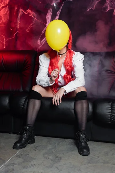 Sexy woman in black knee socks sitting with yellow balloon on dark background with smoke — Stock Photo