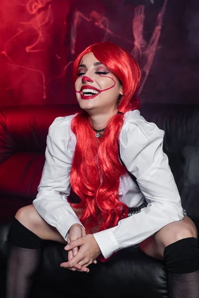 Excited redhead woman with closed eyes and halloween makeup laughing on dark background with spiderweb — Stock Photo