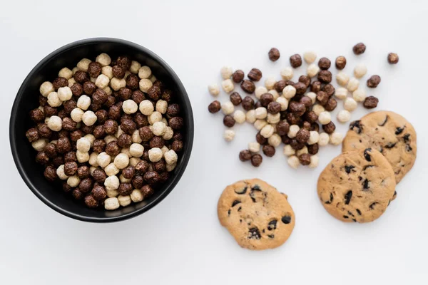 Vue du dessus des boules de céréales dans un bol près de biscuits aux pépites de chocolat isolés sur blanc — Photo de stock