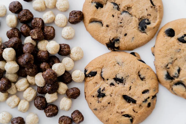 Vista dall'alto di palline di cereali con aromi di vaniglia e cioccolato vicino deliziosi biscotti isolati su bianco — Foto stock