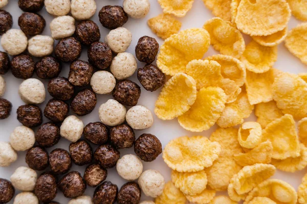 Primer plano de bolas de cereales con diferentes sabores cerca de copos de maíz aislados en blanco - foto de stock