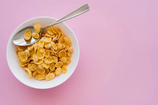 Vista superior del tazón con hojuelas de maíz y cuchara sobre fondo rosa - foto de stock