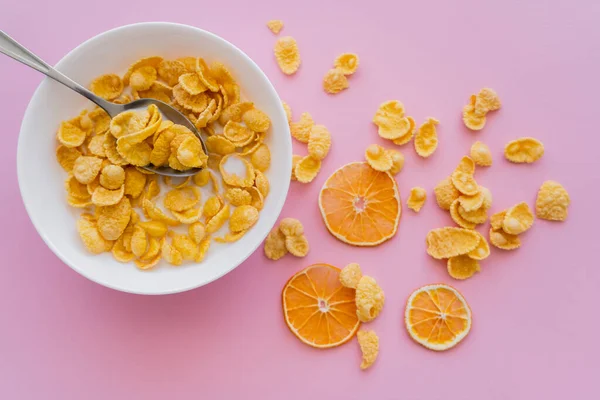 Vue de dessus des oranges séchées près du bol avec des flocons de maïs et du lait biologique sur rose — Photo de stock