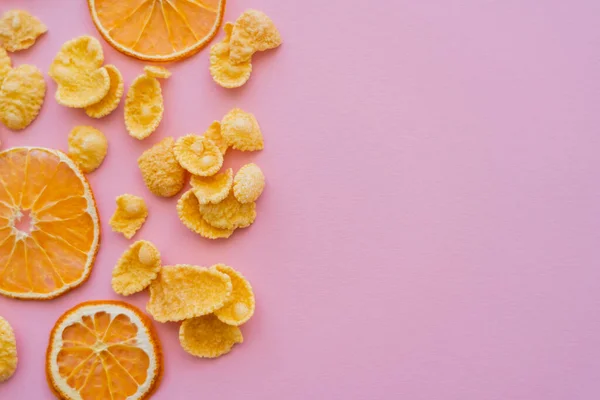 Vue de dessus des oranges séchées près de flocons de maïs savoureux sur fond rose — Photo de stock