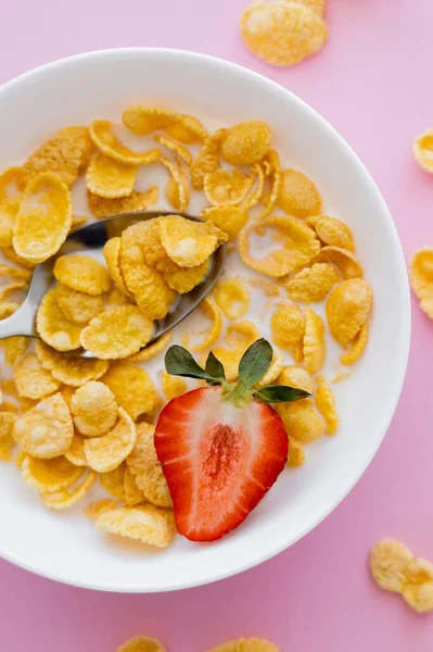 Top view of bowl with tasty corn flakes and sliced strawberry on pink — Stock Photo