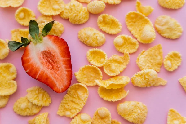 Vista da vicino di fragola fresca affettata intorno croccante fiocchi di mais su rosa — Foto stock