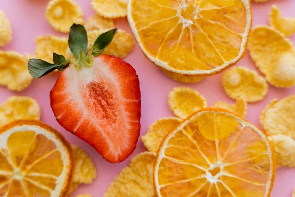 Vista da vicino della fragola fresca tagliata a fette intorno a fiocchi di mais croccanti e arance secche su rosa — Foto stock