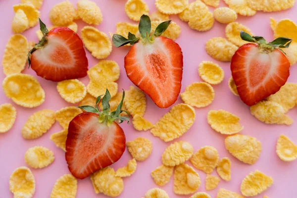 Vista de cerca de fresas frescas en rodajas alrededor de hojuelas de maíz crujientes en rosa - foto de stock