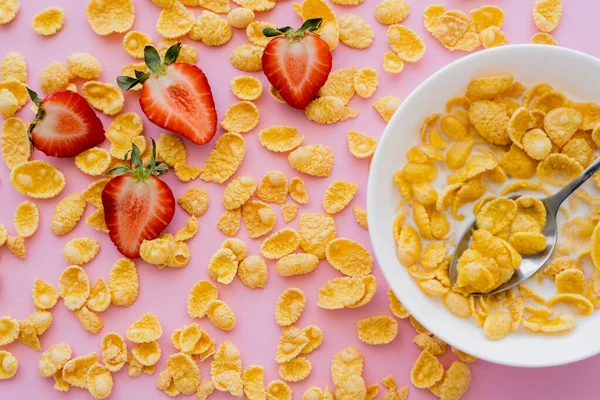 Close up view of fresh sliced strawberries around crispy corn flakes and bowl on pink — Stock Photo