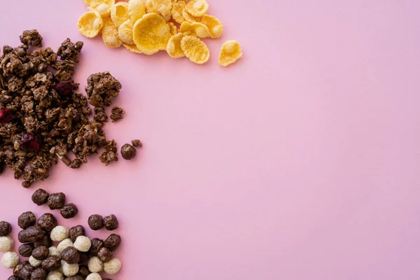 Вид сверху кукурузных хлопьев возле зерновых шариков с ванильным и шоколадным вкусами и мюсли, выделенных на розовом — стоковое фото