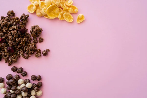 Top view of corn flakes near cereal balls with vanilla and chocolate flavors and granola isolated on pink — Stock Photo