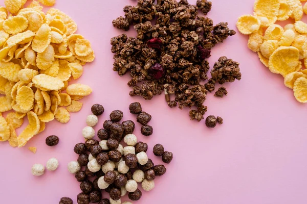 Vista superior de copos de maíz cerca de bolas de cereales con sabores de vainilla y chocolate y sabrosa granola aislada en rosa - foto de stock