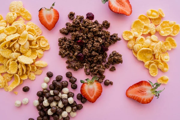 Vista superior de diferentes flocos de milho perto de granola saborosa e morangos frescos isolados em rosa — Fotografia de Stock