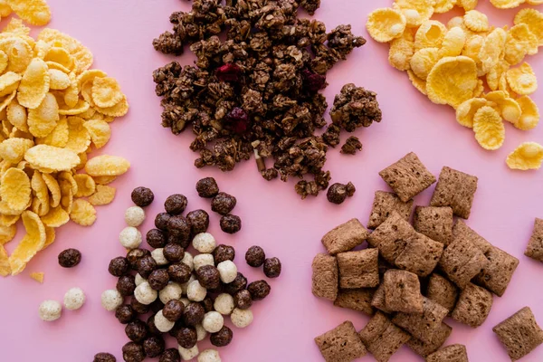 Vista superior de diferentes y sabrosos cereales cerca de granola crujiente aislado en rosa - foto de stock
