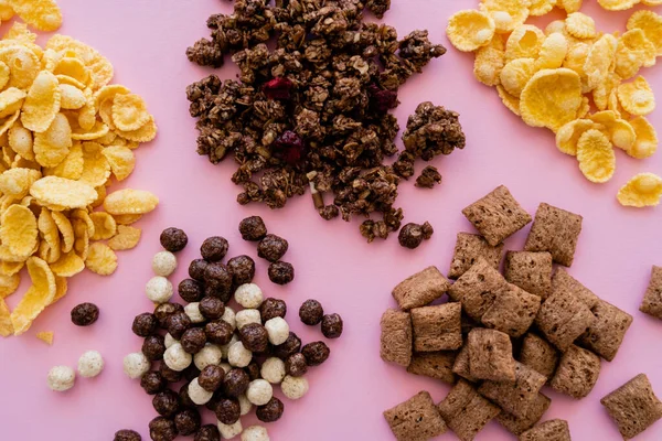 Draufsicht auf verschiedene und leckere Getreidesorten in der Nähe von knusprigem Müsli isoliert auf rosa — Stockfoto