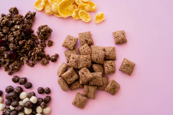 Vista superior de varios cereales de desayuno copos de maíz, soplos, bolas y granola en rosa - foto de stock