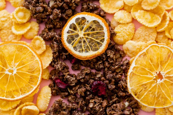 Vista superior de copos de maíz crujientes y sabrosa granola cerca de naranjas secas en rosa - foto de stock