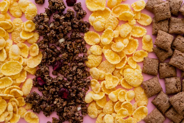 Top view of various breakfast cereal corn flakes with puffs and granola on pink — Stock Photo