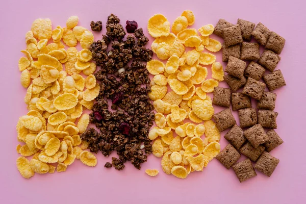 Draufsicht auf verschiedene Frühstückscerealien Cornflakes mit Windbeutel und Müsli isoliert auf rosa — Stockfoto