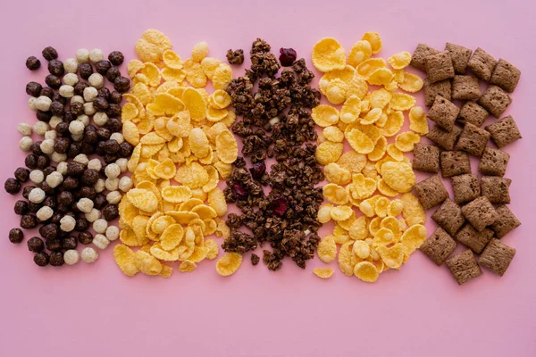 Vista superior de una variedad de cereales de desayuno, copos de maíz y granola crujiente aislado en rosa - foto de stock