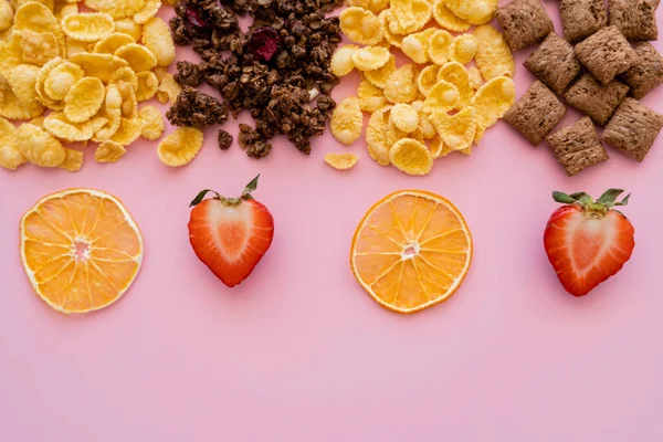 Вид зверху різноманітного сніданку кукурудзяні пластівці та хрусткі граноли поблизу фруктів ізольовані на рожевому — стокове фото