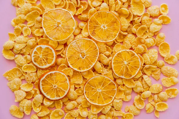 Vue de dessus des oranges séchées sur le dessus des flocons de maïs croustillants du petit déjeuner isolés sur rose — Photo de stock