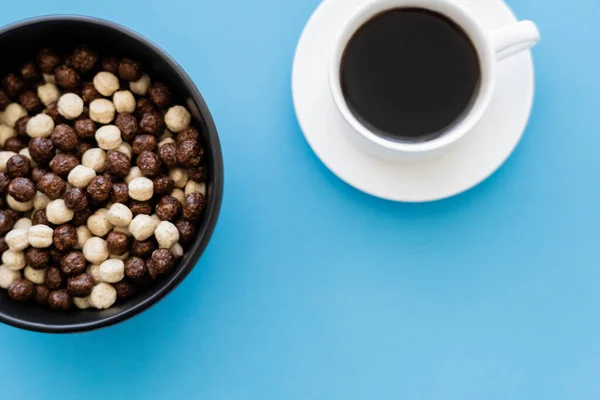 Vista superior da tigela com saborosas bolas de cereais perto da xícara de café preto isolado em azul — Fotografia de Stock