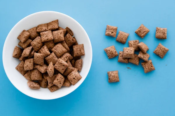 Vista superior de las bocanadas de cereales de chocolate y tazón blanco aislado en azul - foto de stock