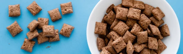 Top view of chocolate cereal puffs and white bowl isolated on blue, banner — Stock Photo