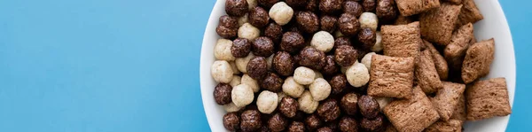 Vista dall'alto della ciotola con gustose palline di cereali e soffi isolati su blu, banner — Foto stock