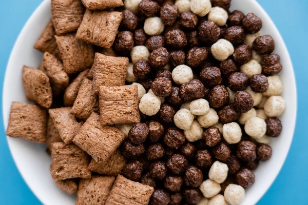 Vista da vicino della ciotola con gustose palline di cereali e soffi isolati su blu — Foto stock