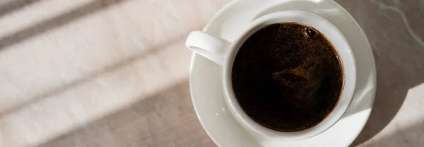 Top view of cup of black coffee and white saucer on marble surface, banner — Stock Photo