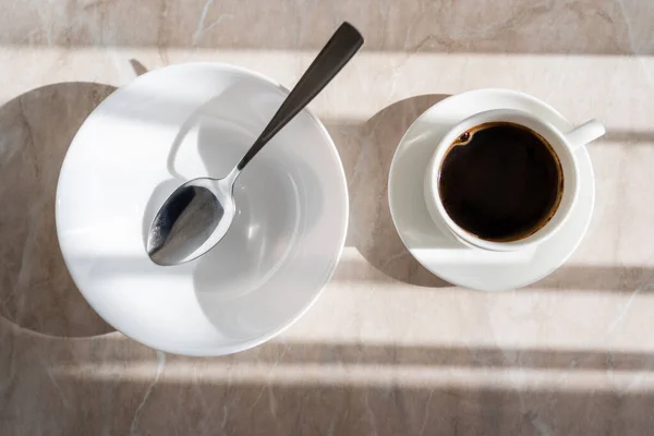 Vista superior da xícara de café preto perto do pires branco com colher na superfície de mármore — Fotografia de Stock